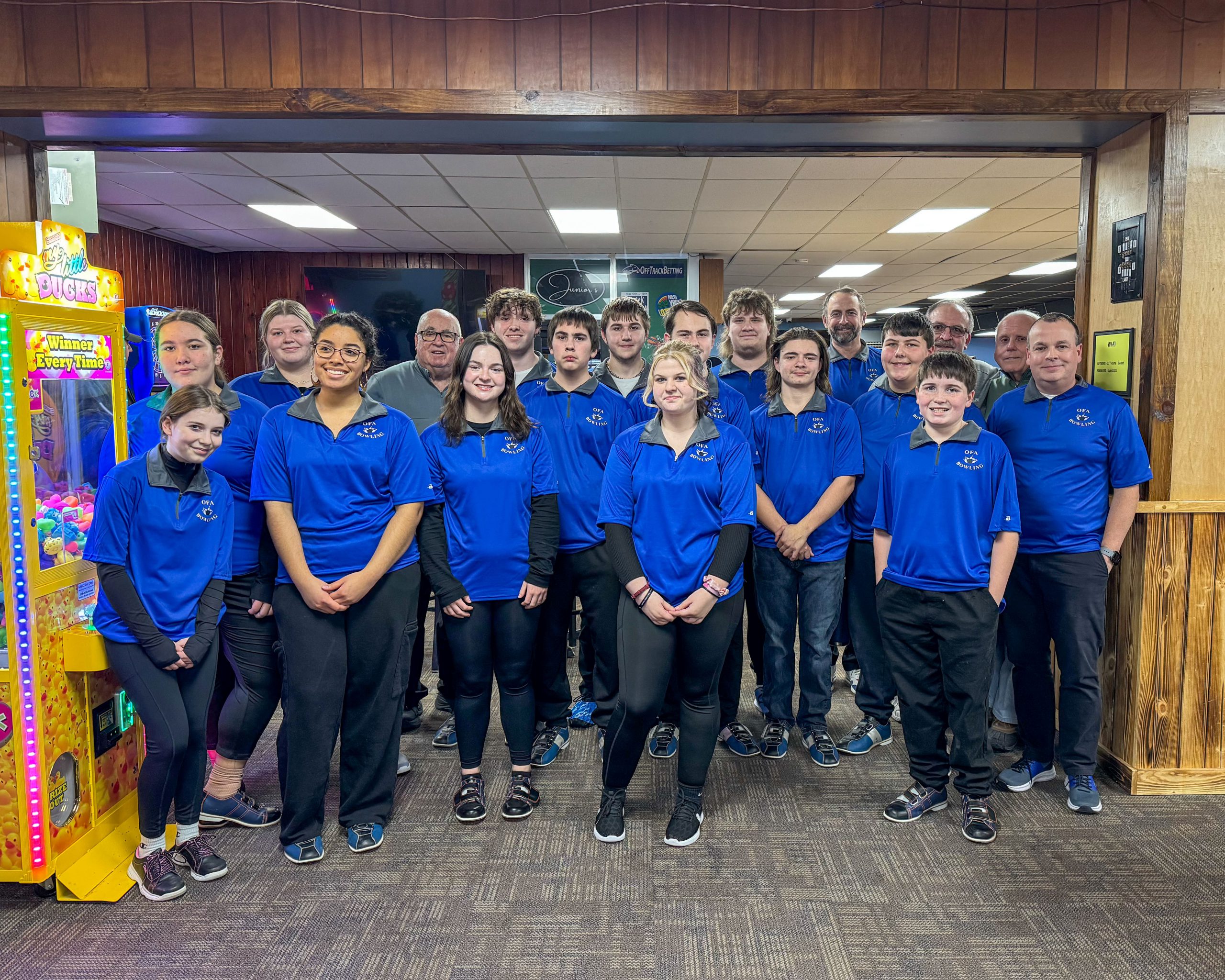 large group of teenage students on a bowling team wearing matching blue bowling shirts and black pants, posing and smiling