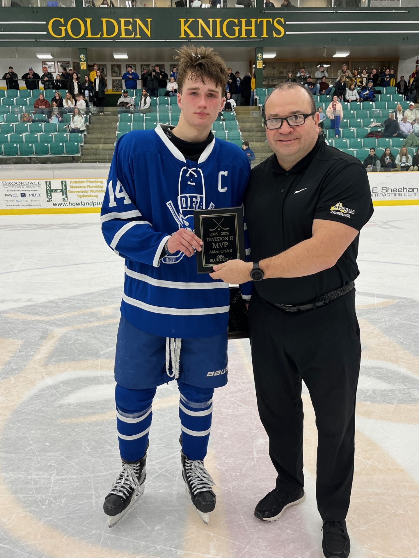 High school male hockey player receiving a plaque from an adult male
