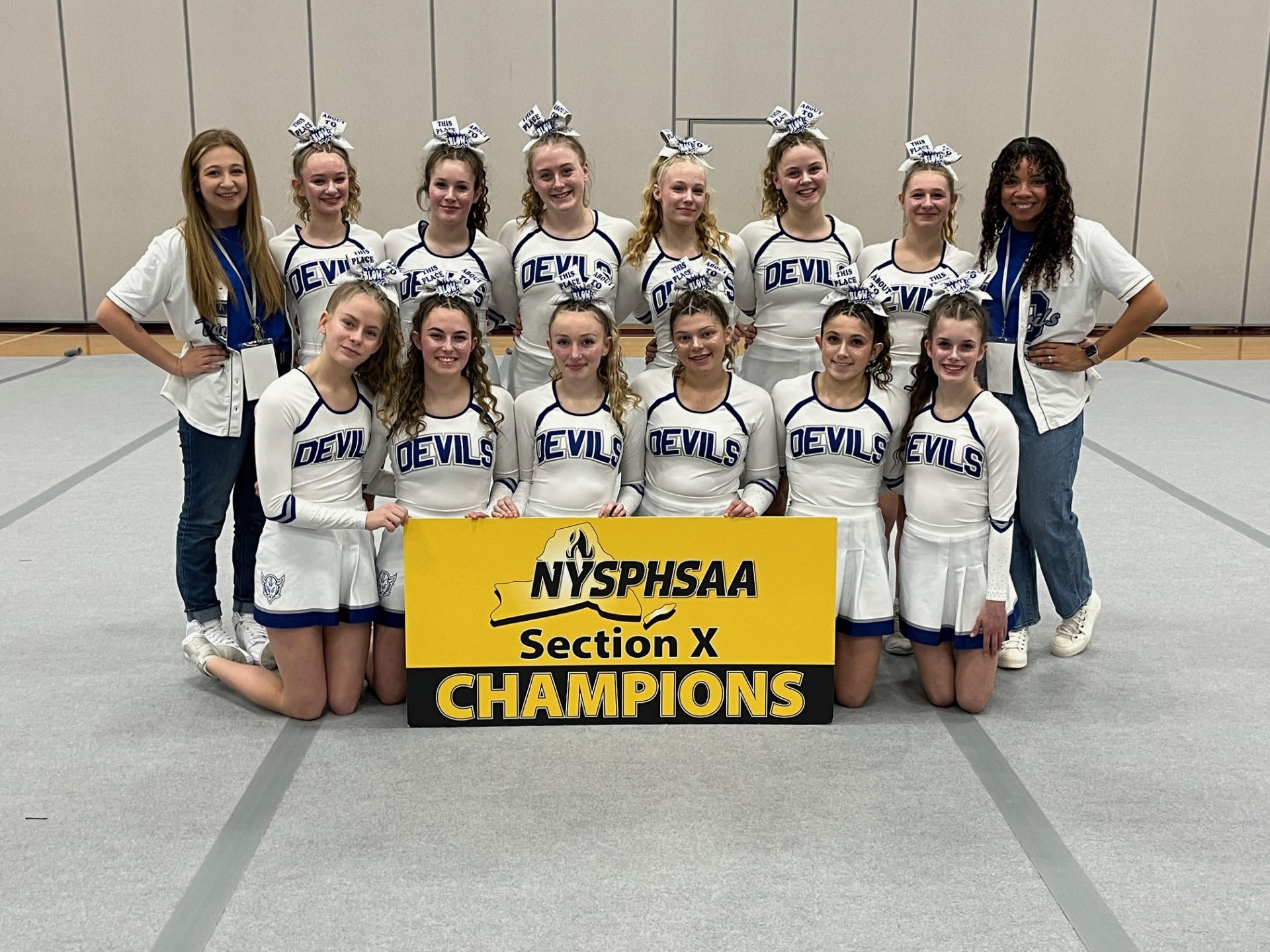 Small group of female high school students with female coaches in white uniforms holding a sign