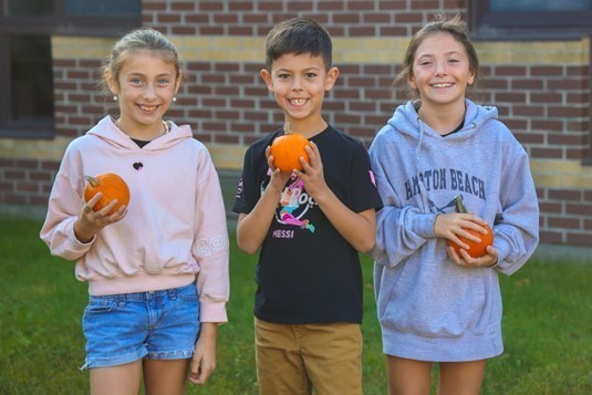Three students happily hold mini pumpkins.