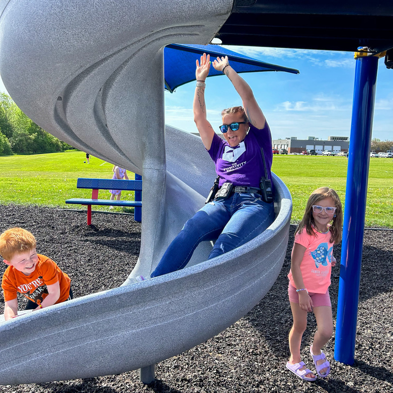 Patrolman Ashley Streeter sliding down a slide at the JFK Elementary playing with students