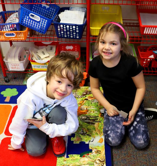Two elementary students kneel working on a floor puzzle.