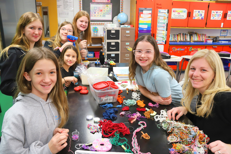 Several students gather at a table with craft supplies and a teacher.