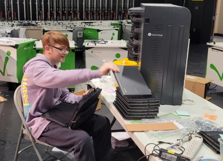 A high school student prepares chromebooks with cases.
