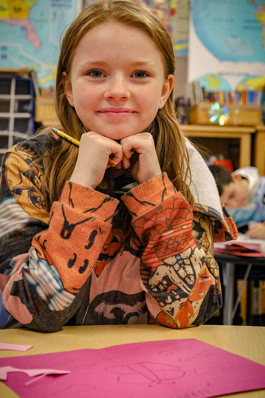 A student rests her chin on her shoulders in a classroom setting.