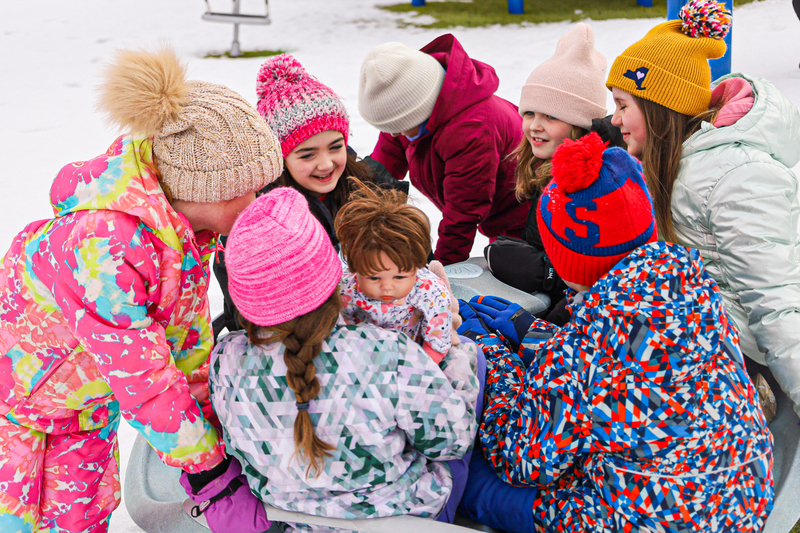 Several students dressed in outerwear crowd around together in the snow.