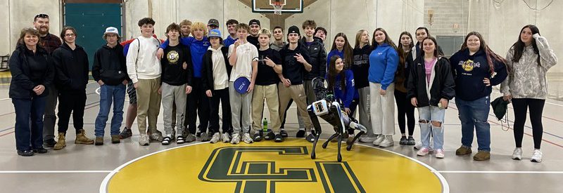 Several high school students pose in a Clarkson gym with a robot dog.