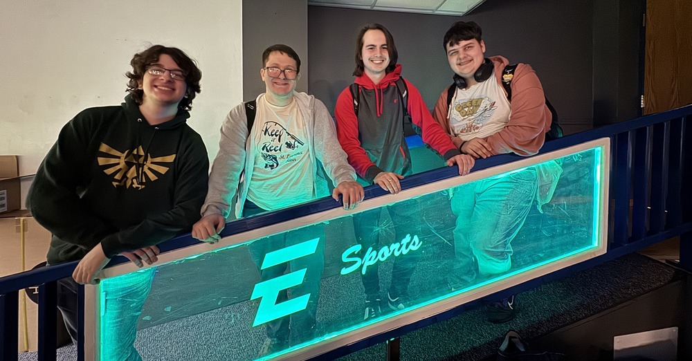 Four high school students pose behind an Esports signs.