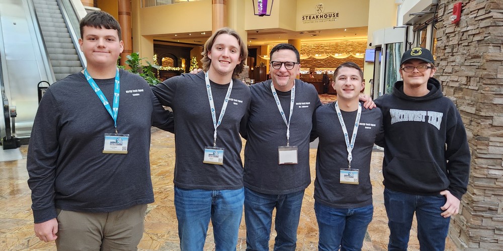 Four OFA students wearing lanyards pose with a teacher.