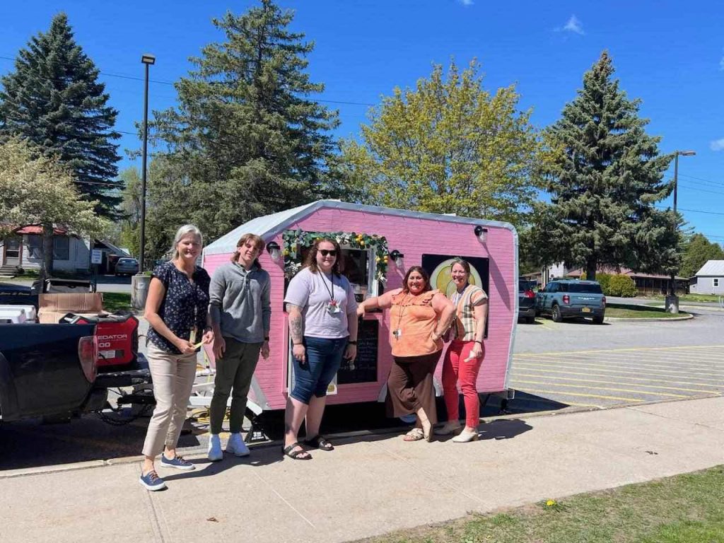 Five adults stand in front of a decorated trailer.