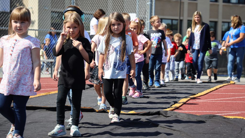 Kindergarteners walk in a line on the outdoor track.