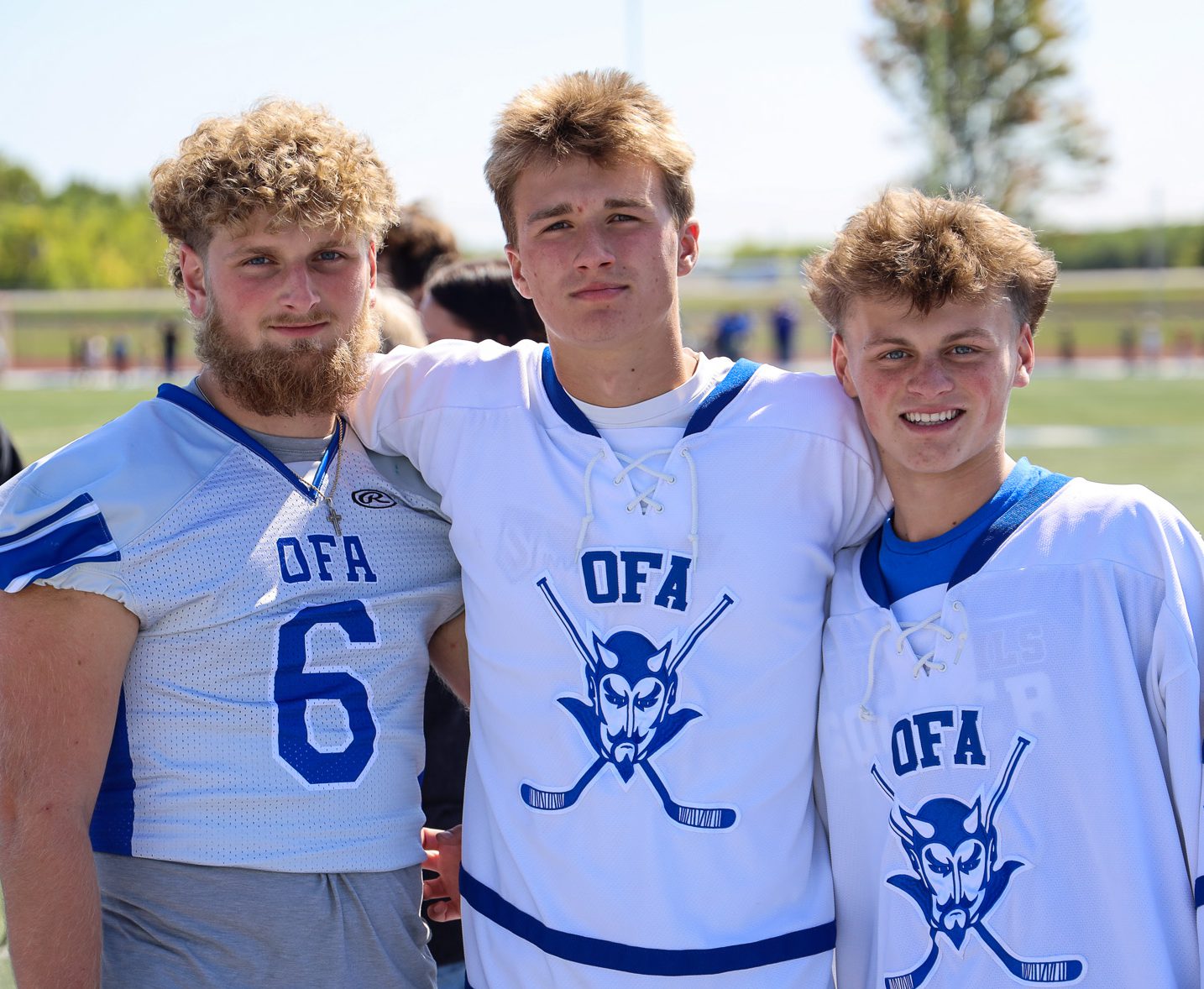 Three OFA students in football gear stand together on the field.