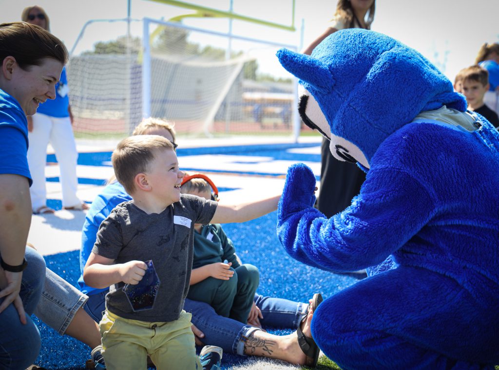 A young student does a high five with the devil mascot.
