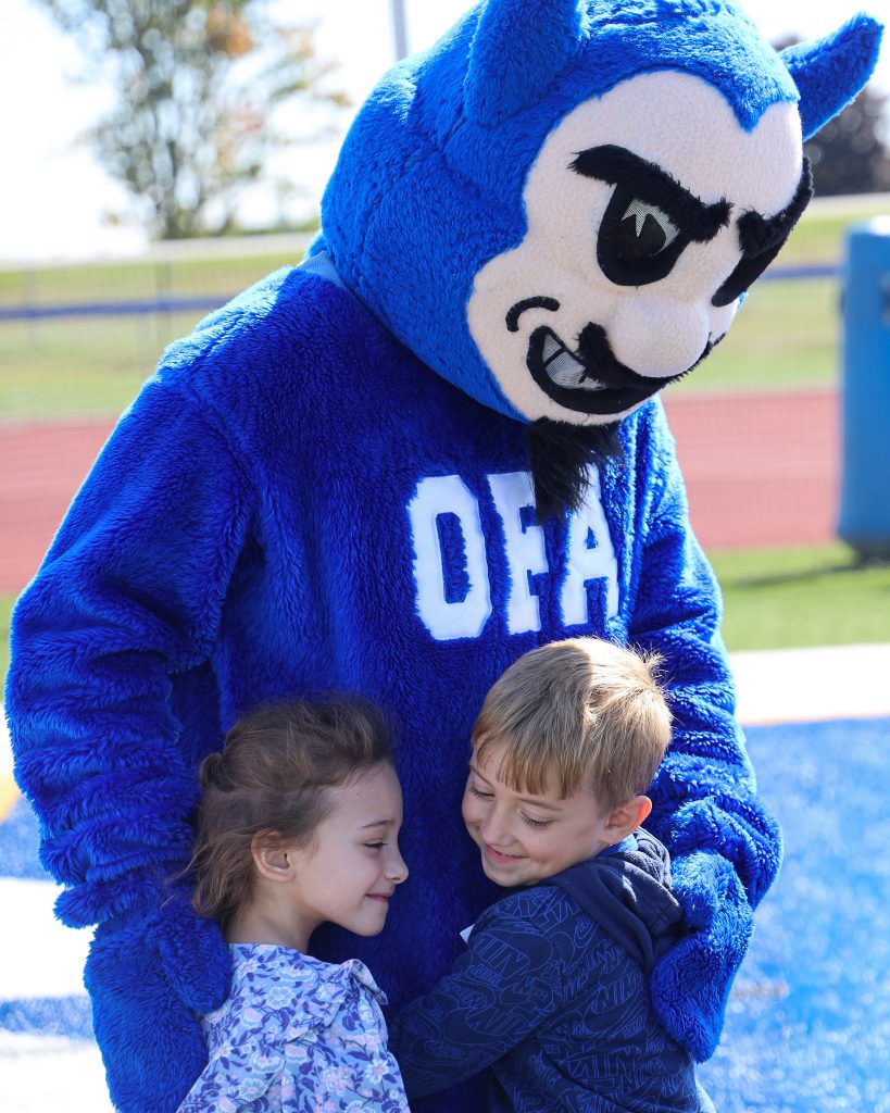 Two kindergarteners hug the devil mascot.