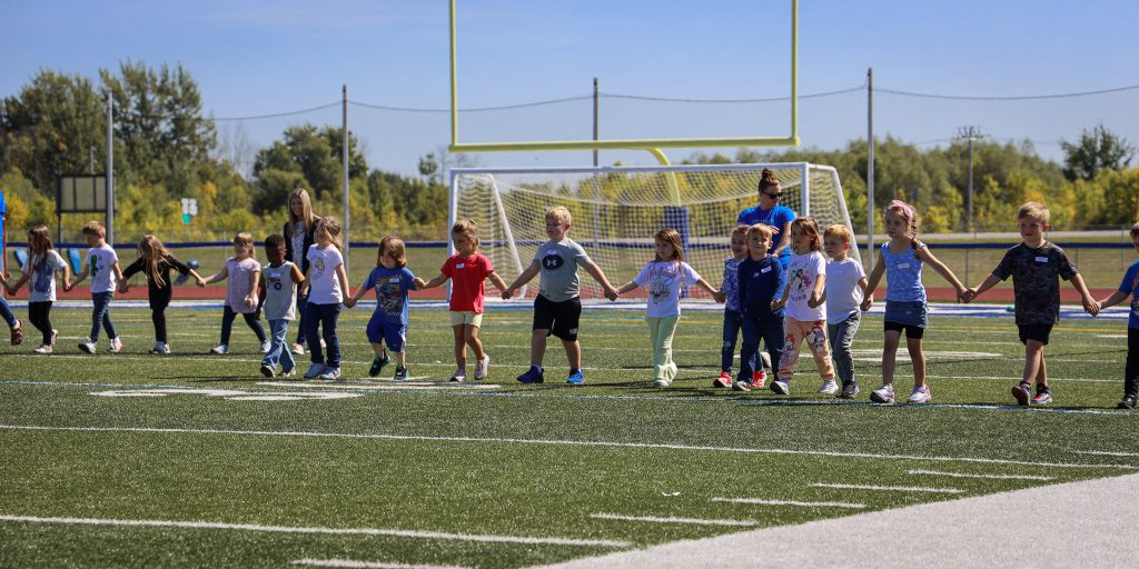 A group of kindergarteners walk across a field.