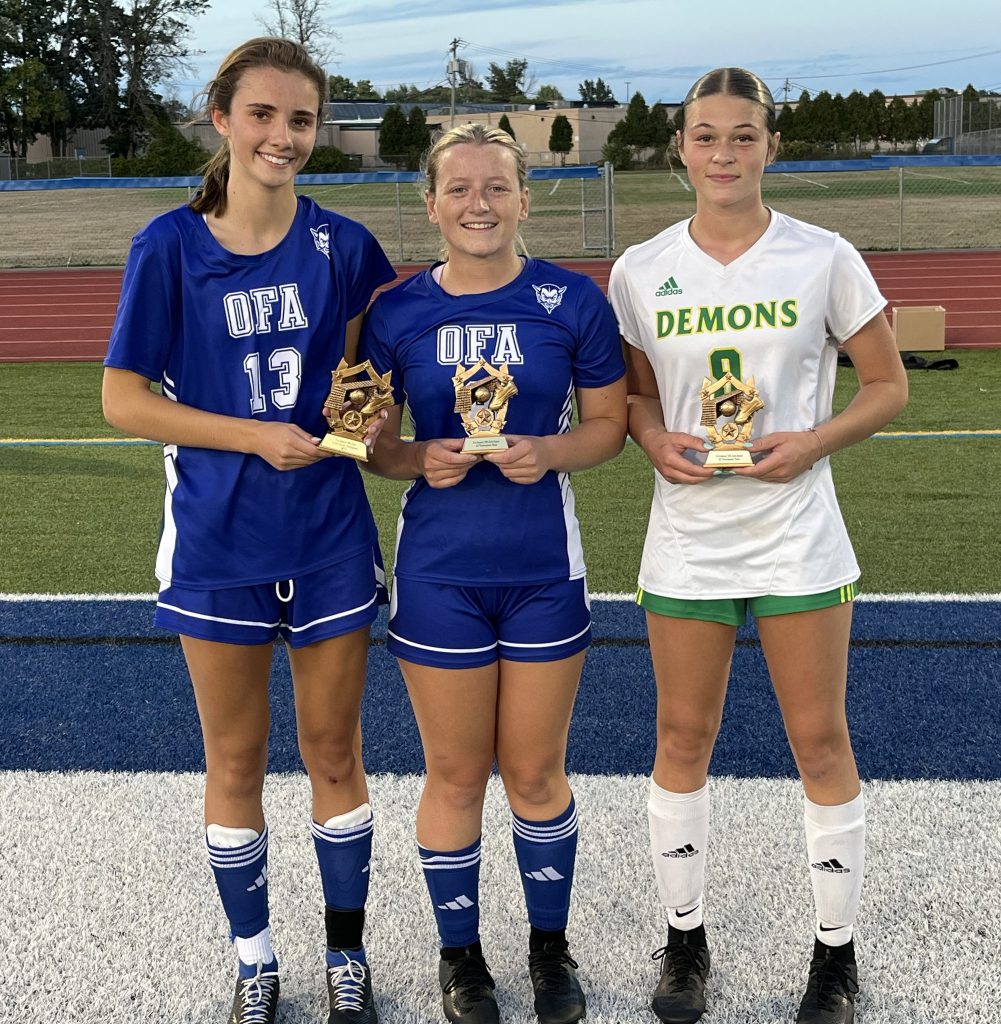 Three girls varsity soccer team members pose with trophies.