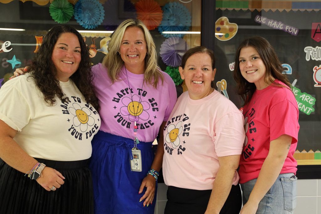 Four teachers smiling while wearing tshirts that say "happy to see your face".