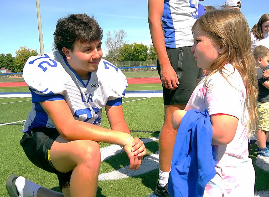 An OFA football player leans down to chat with a kindergartener.