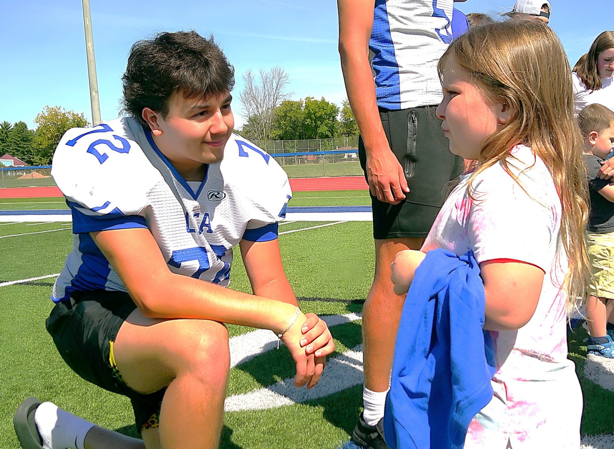 An OFA football player leans down to chat with a kindergartener.