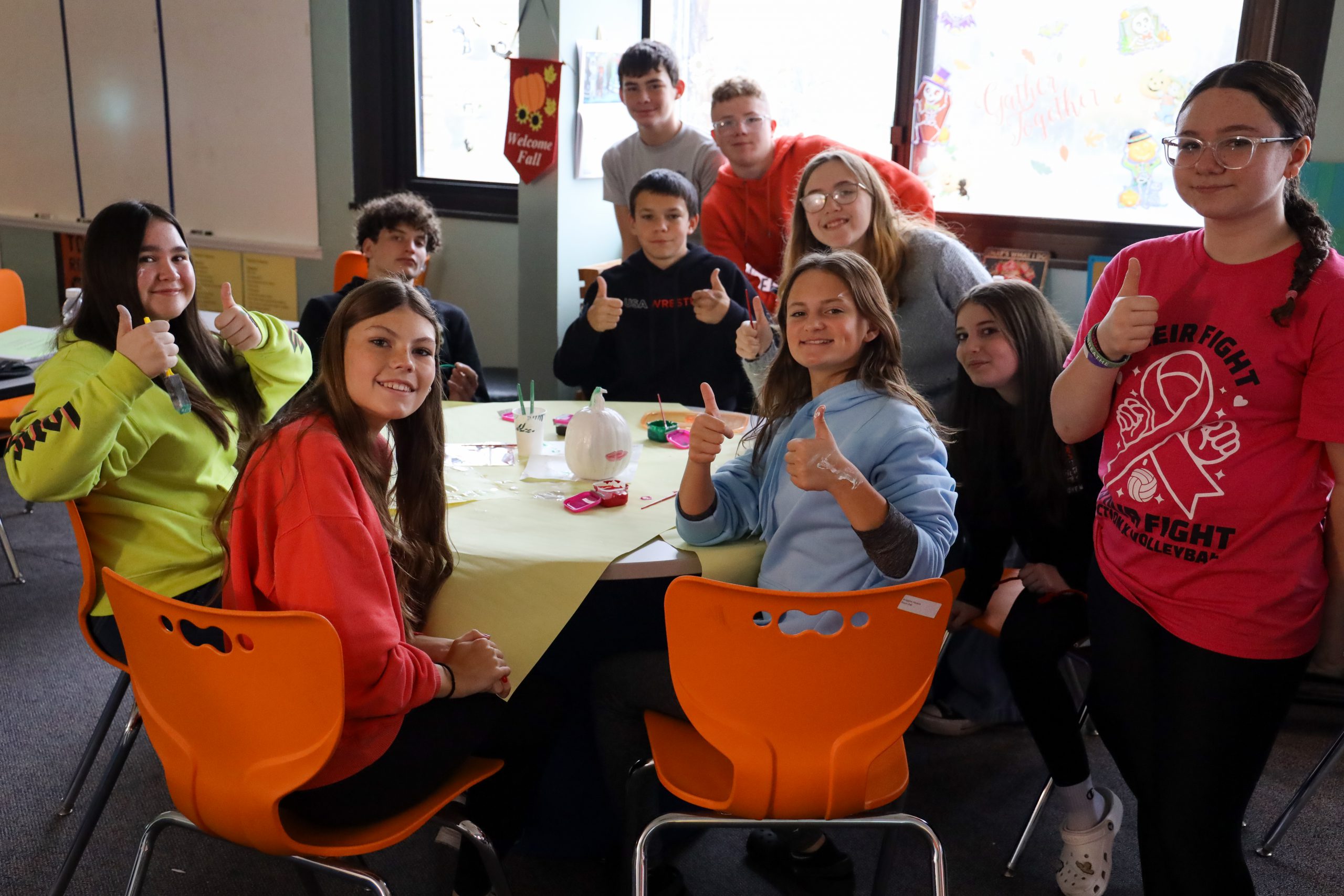 Group of students sitting around a table giving thumb's up