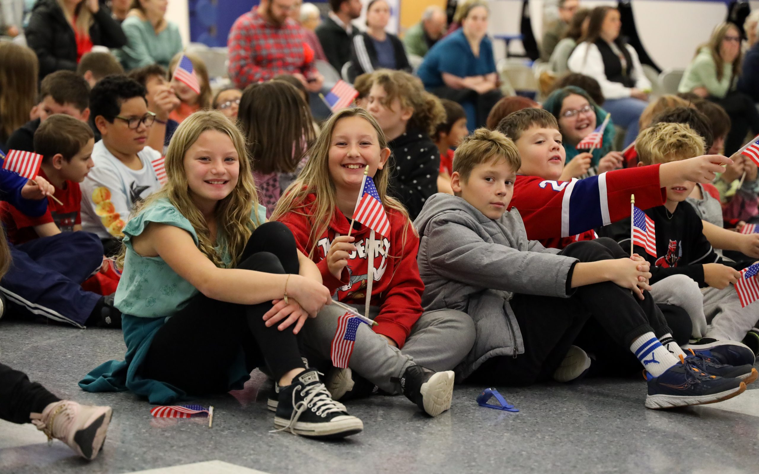 Students smiling with flags in hand during veterans day ceremony