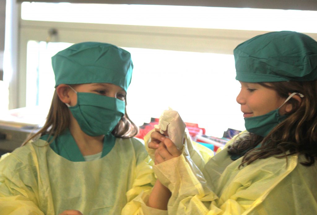 Female elementary students laughing while putting on hospital scrubs and gloves
