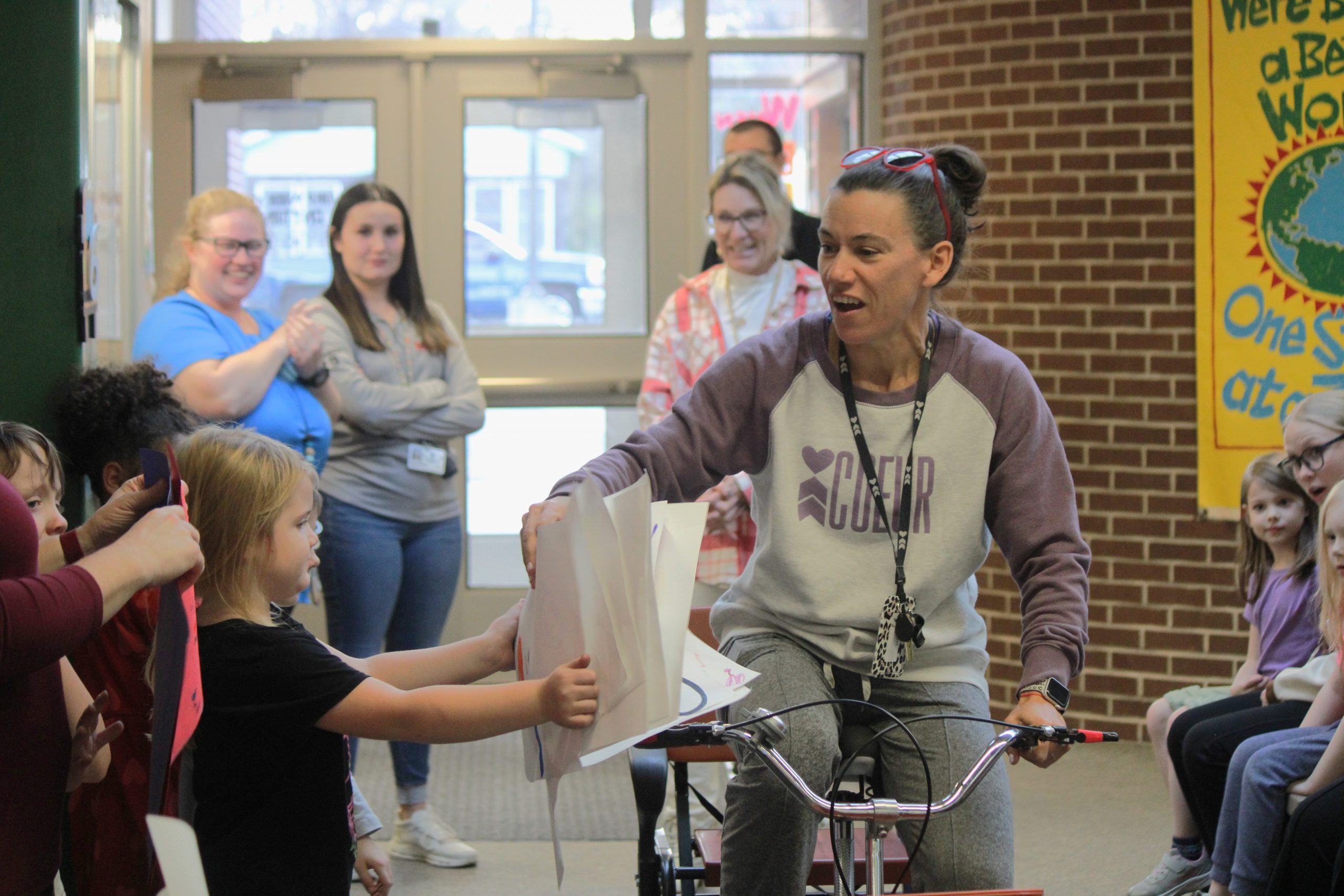 Group of elementary students handing handmade signs to teacher on tricycle