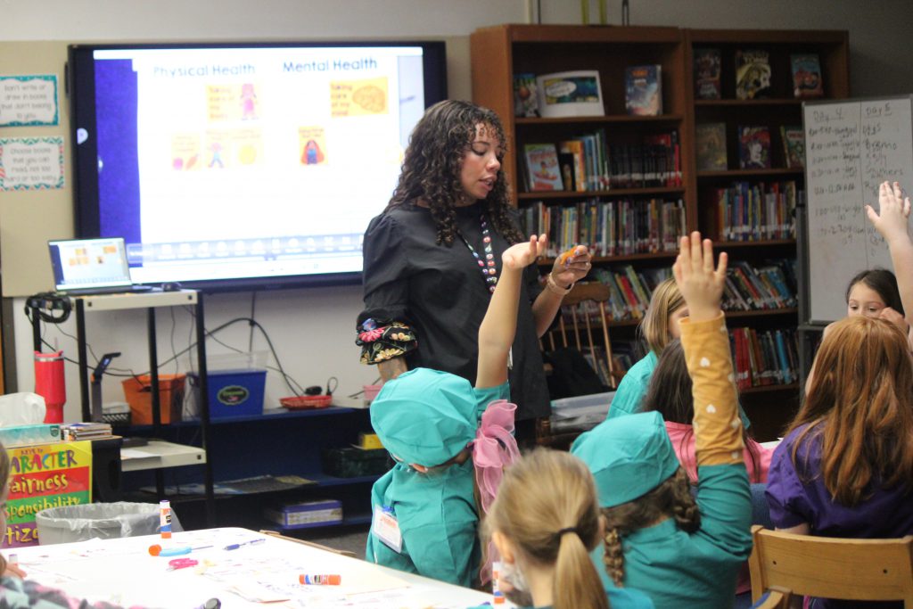 Female school counselor and elementary students raising hands
