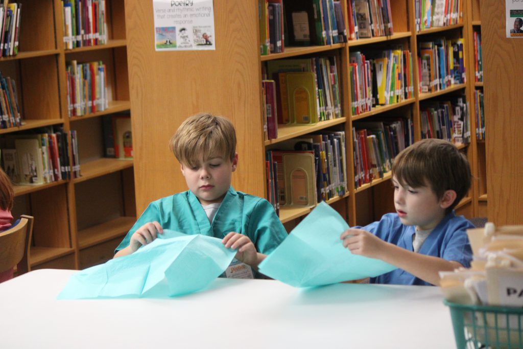 Two male elementary students sitting at a table putting on bibs