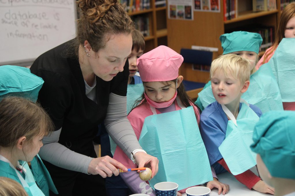 Female dental staff member uses toothbrush to show elementary students an activity
