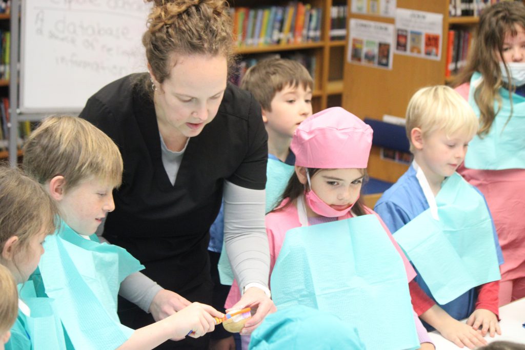 Group of elementary students gathered around female dental staff member