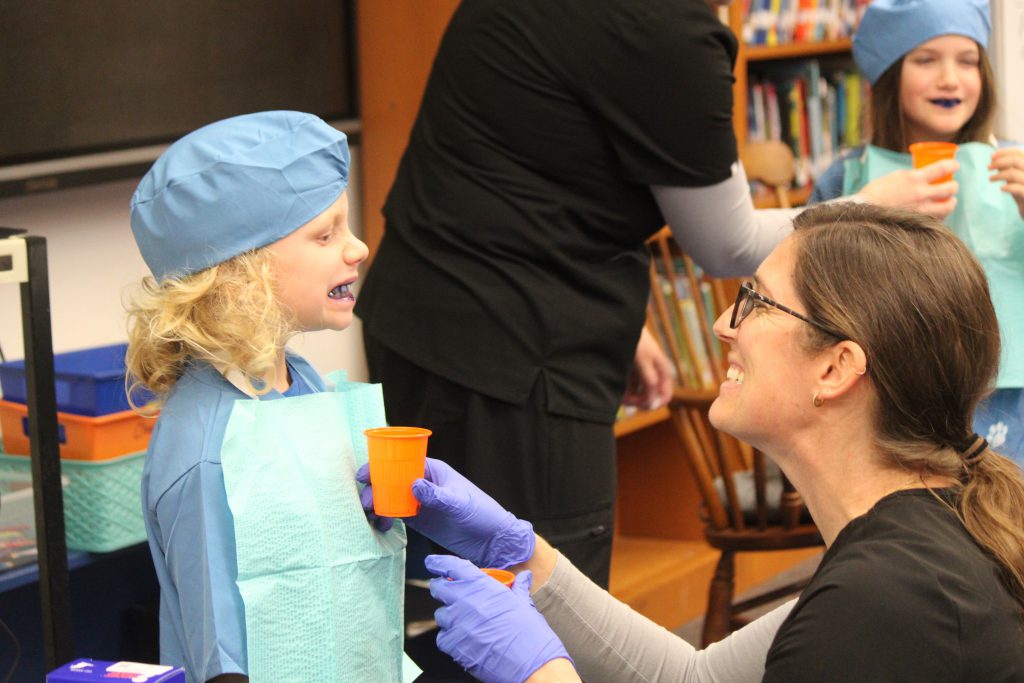 Male elementary student shows female dental staff member his teeth