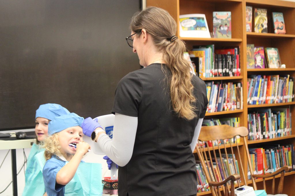 Female dental staff assists male elementary student in brushing his teeth