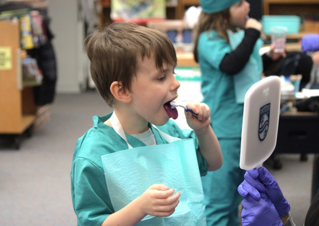 Male elementary student brushing teeth and looking in mirror
