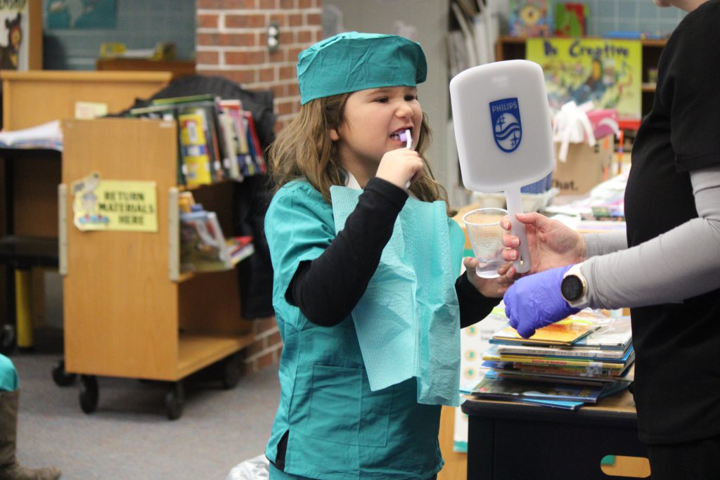 Female elementary student brushing teeth and looking in mirror