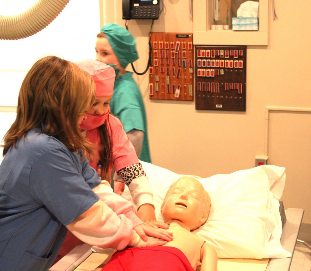 Female elementary students give CPR to doll