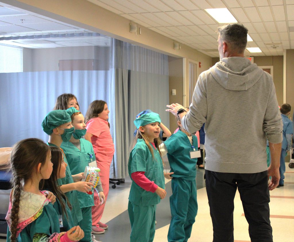 Group of elementary students participate in activity with supervision of male hospital staff member
