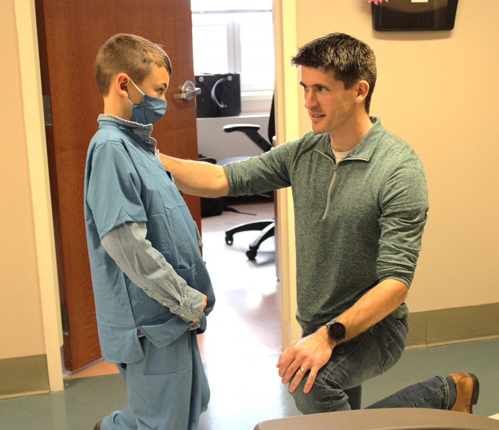 Male elementary student balancing with help of hospital staff member