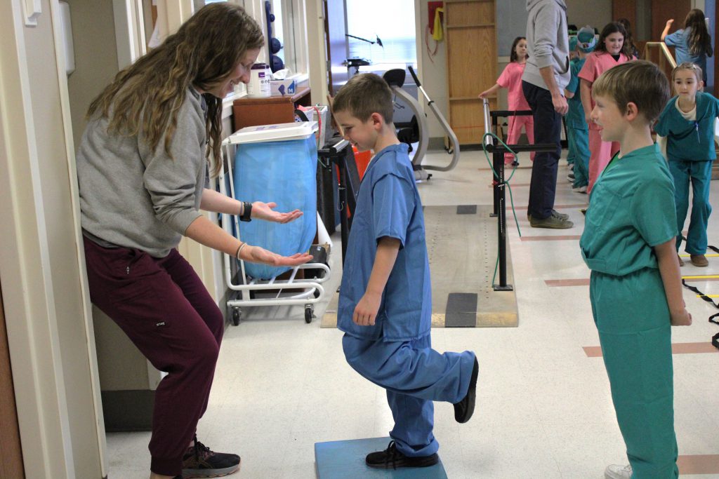 Male elementary student balancing with female hospital staff member