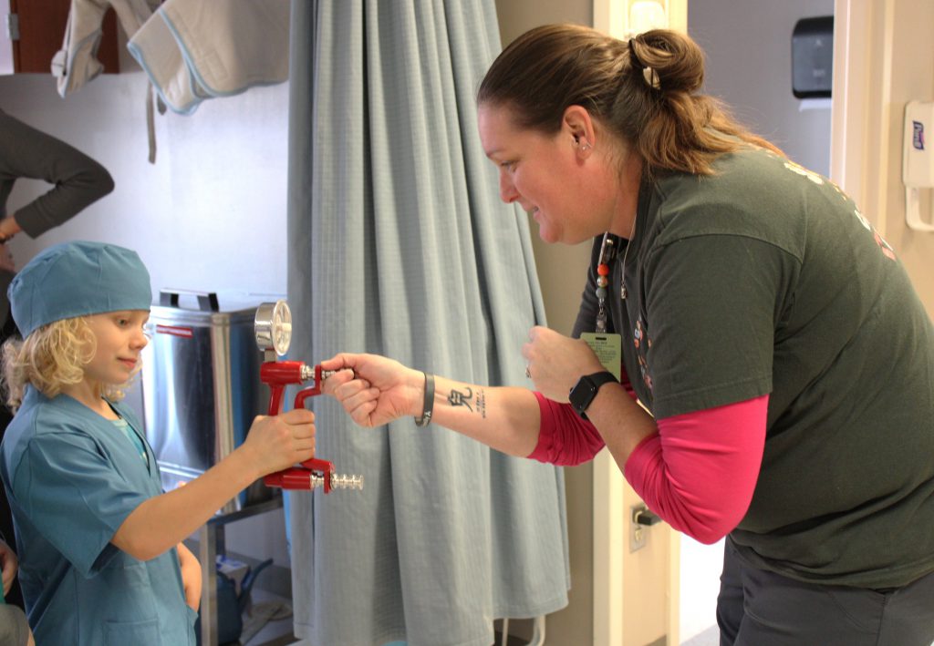Male elementary student using medical device with female hospital staff member