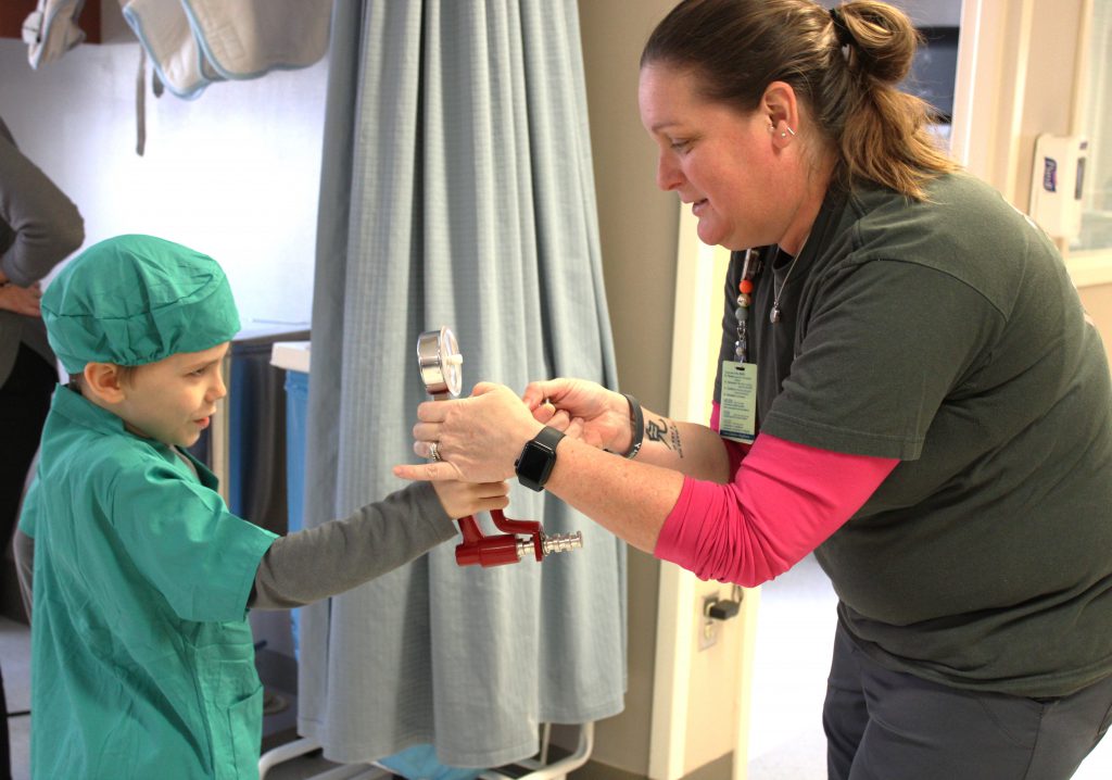 Male elementary student using medical device with female hospital staff member