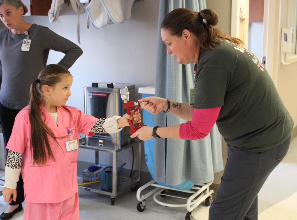 Female elementary student using medical device with female hospital staff member