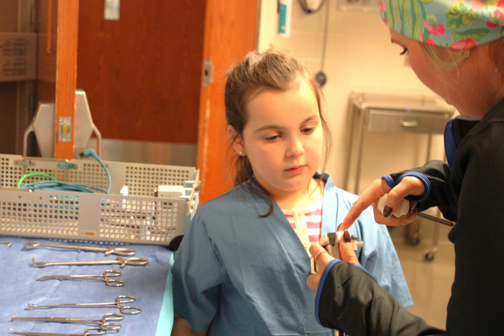 Female elementary student learning how to use a medical device from a hospital staff member