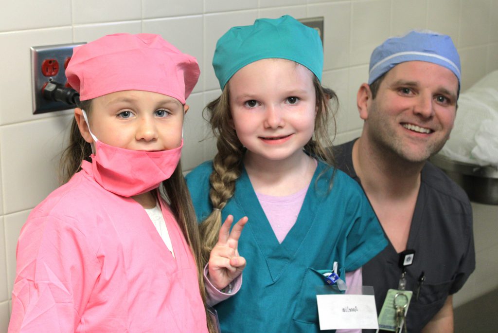 Two female elementary students with a male hospital staff member