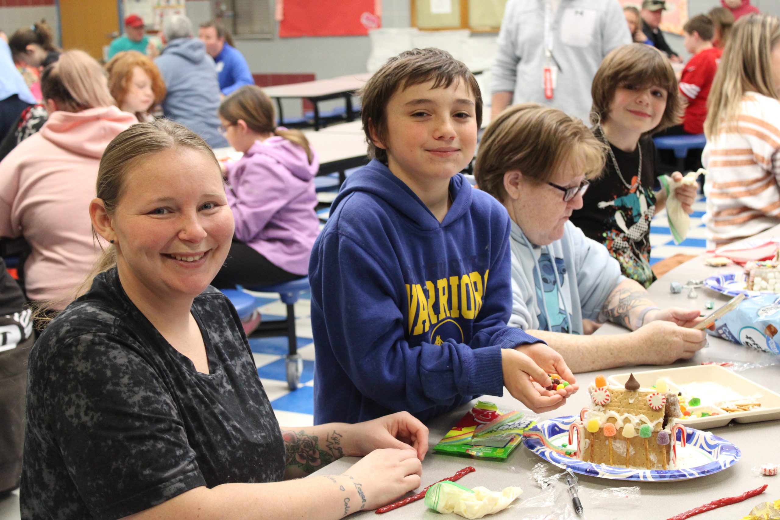 Male elementary student and adult female smiling and making gingerbread house