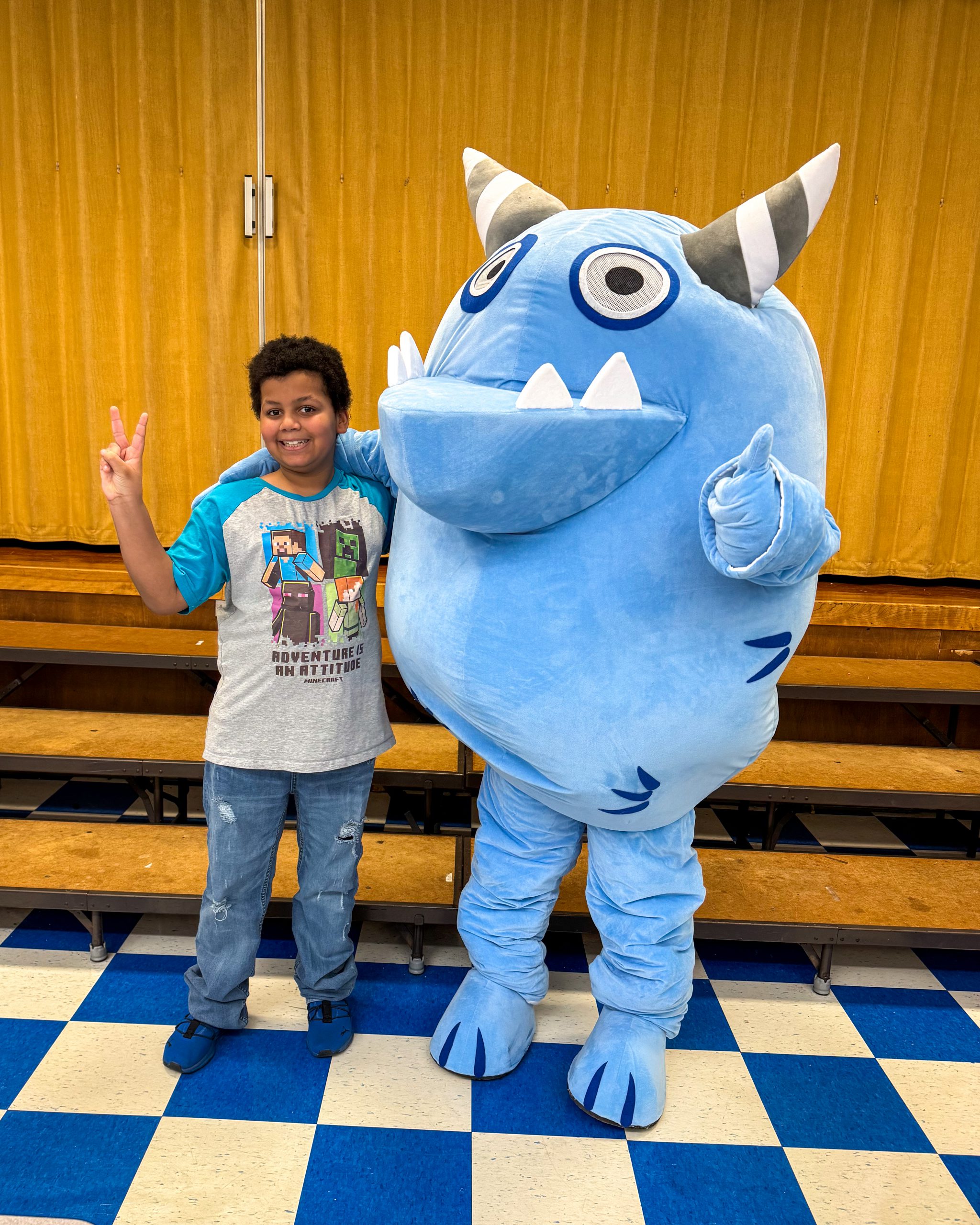 Male elementary student giving the peace sign with a blue monster mascot