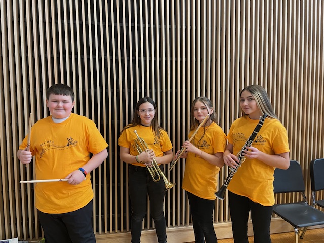 Small group of elementary band students wearing yellow and holding musical instruments