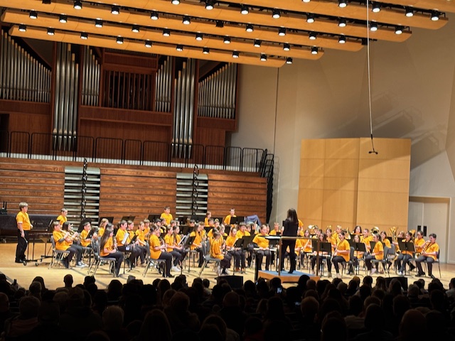 Large group of elementary band students performing on stage wearing yellow