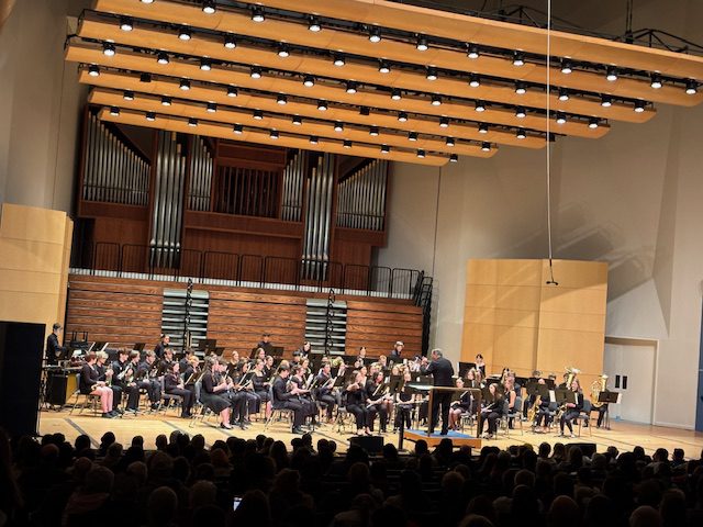 Large group of band students wearing black and performing on stage