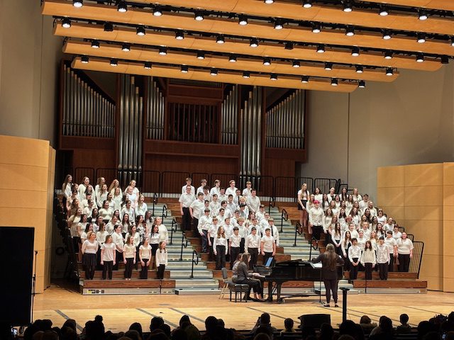 Large group of choral students wearing white and black performing on stage